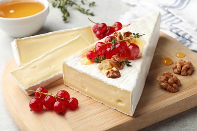 Brie cheese served with red currants, walnuts and honey on table, closeup