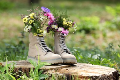 Beautiful flowers in boots on stump outdoors, space for text