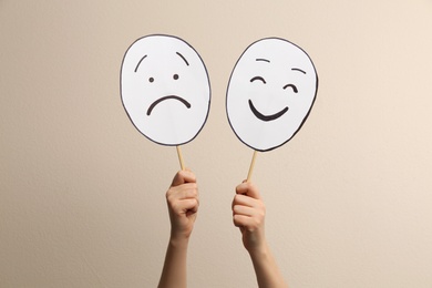 Woman with sad and happy paper faces on beige background, closeup