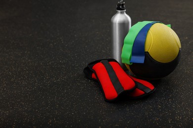 Medicine ball, bottle, weighting agents and elastic bands on floor, space for text