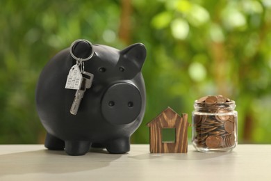 Photo of Piggy bank with key, house model and coins in glass jar on wooden table outdoors. Saving money concept