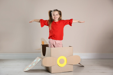 Cute little child playing with cardboard plane near beige wall