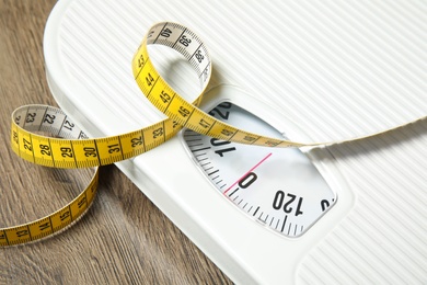 Scales and measuring tape on wooden background, closeup. Weight loss
