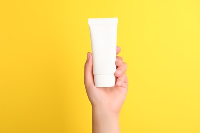 Woman holding tube of face cream on yellow background, closeup