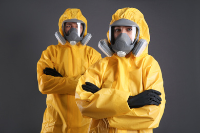 Man and woman wearing chemical protective suits on grey background. Virus research