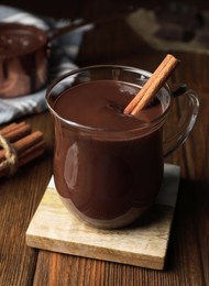 Cup of delicious hot chocolate with cinnamon stick on wooden table