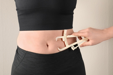 Nutritionist measuring woman's body fat layer with caliper on beige background, closeup