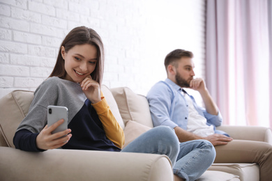 Young woman with smartphone ignoring her boyfriend at home. Relationship problems
