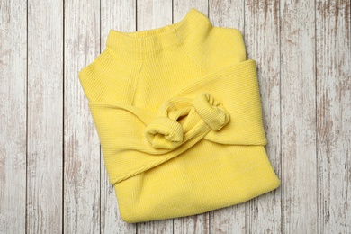 Photo of Beautiful yellow warm sweater on white wooden table, top view