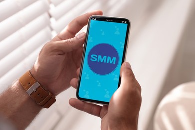 SMM (Social Media Marketing) concept. Man using smartphone near window indoors, closeup