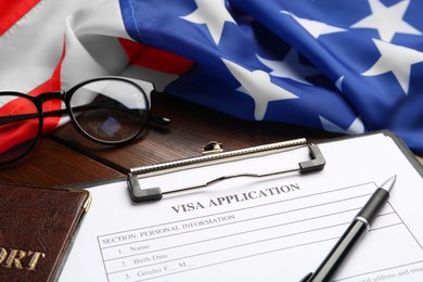 Visa application form for immigration, passport and American flag on wooden table, closeup