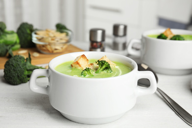 Delicious broccoli cream soup with croutons served on white wooden table indoors