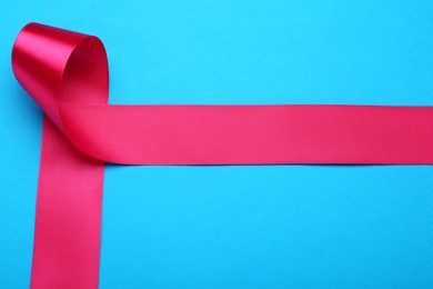 Beautiful pink ribbon on light blue background, top view