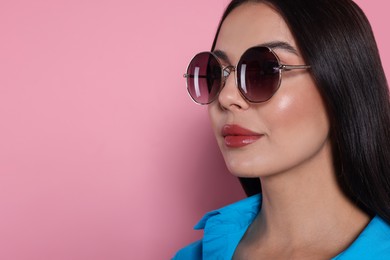 Attractive serious woman in fashionable sunglasses against pink background, closeup. Space for text