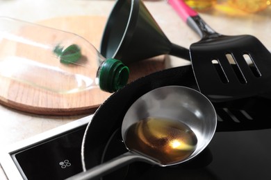 Frying pan of used cooking oil with ladle, empty bottle and funnel in kitchen, closeup