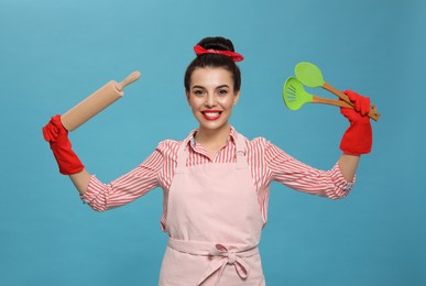 Young housewife with cooking utensils on light blue background