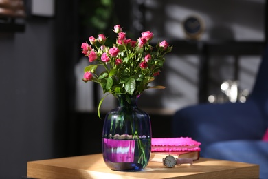 Glass vase with fresh flowers and wristwatch on wooden table
