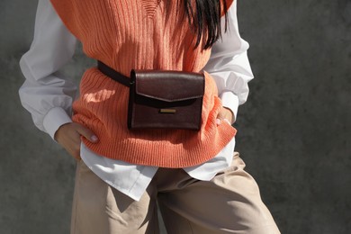 Young woman with stylish waist bag near grey wall outdoors, closeup