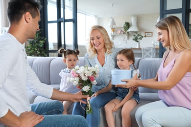 Happy family with little children congratulating mature woman in living room