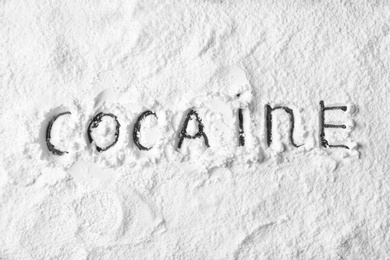 Word Cocaine written on white powder as background, top view