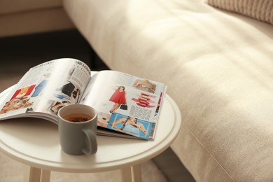 Fashion magazine and cup of hot drink on white table in living room