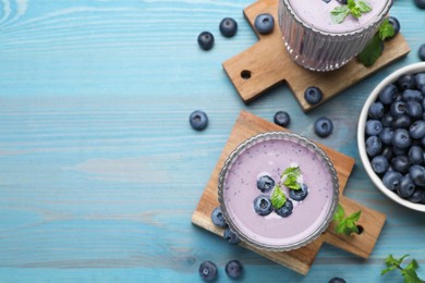 Glasses of blueberry smoothie with mint and fresh berries on light blue wooden table, flat lay. Space for text