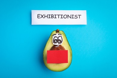 Photo of Avocado with drawn face and word exhibitionist on light blue background, flat lay