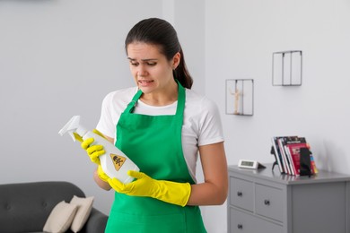 Woman looking at bottle of toxic household chemical with warning sign indoors