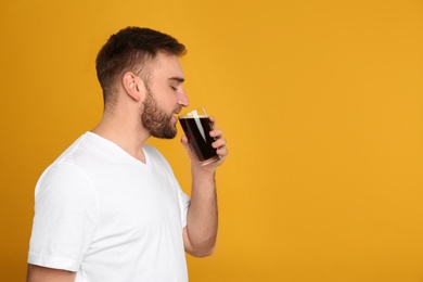 Handsome man with cold kvass on yellow background, space for text. Traditional Russian summer drink