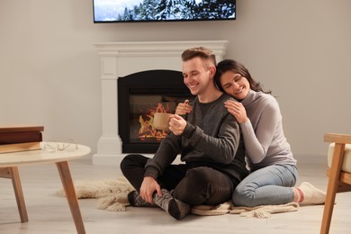 Happy lovely couple with hot drinks spending time together near fireplace at home
