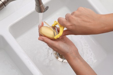 Woman peeling potato over kitchen sink with garbage disposal at home, closeup