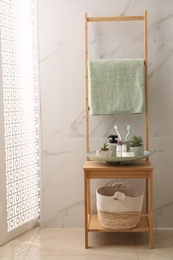 Holder with toothbrushes, different toiletries and plants on wooden rack in bathroom