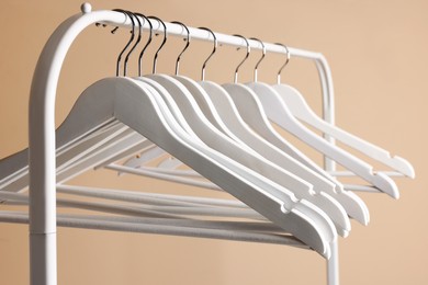 White clothes hangers on metal rack against beige background, closeup