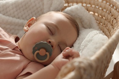 Cute little baby with pacifier sleeping in wicker crib, closeup