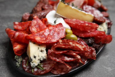 Photo of Tasty salami and other delicacies served on grey table, closeup