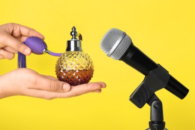 Woman making ASMR sounds with microphone and perfume on yellow background, closeup