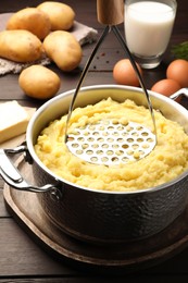 Mashing potatoes in pot on wooden table