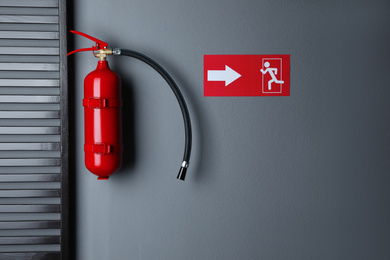 Fire extinguisher and emergency exit sign on grey wall indoors