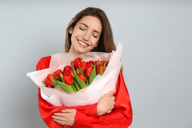Happy woman with red tulip bouquet on light grey background, space for text. 8th of March celebration