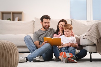 Happy parents with their child reading book on floor at home