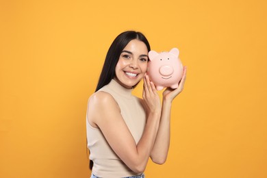 Photo of Happy young woman with piggy bank on orange background