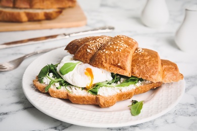 Delicious croissant with arugula and egg on white marble table, closeup
