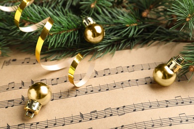 Fir branches, golden streamer and balls on Christmas music sheets, closeup
