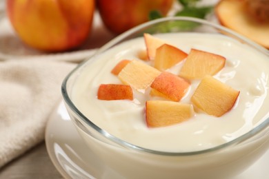 Delicious yogurt with fresh peach in glass bowl on table, closeup