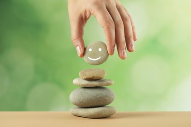 Woman putting stone with drawn happy face onto stack against blurred background, closeup. Zen concept