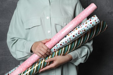 Woman holding different colorful wrapping paper rolls on grey background, closeup