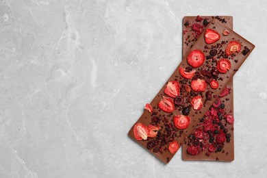 Photo of Chocolate bars with freeze dried berries on grey marble table, top view. Space for text