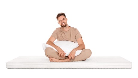 Smiling man with pillow sitting on soft mattress against white background