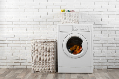 Modern washing machine and laundry baskets near white brick wall