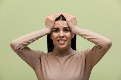 Woman suffering from migraine on light green background